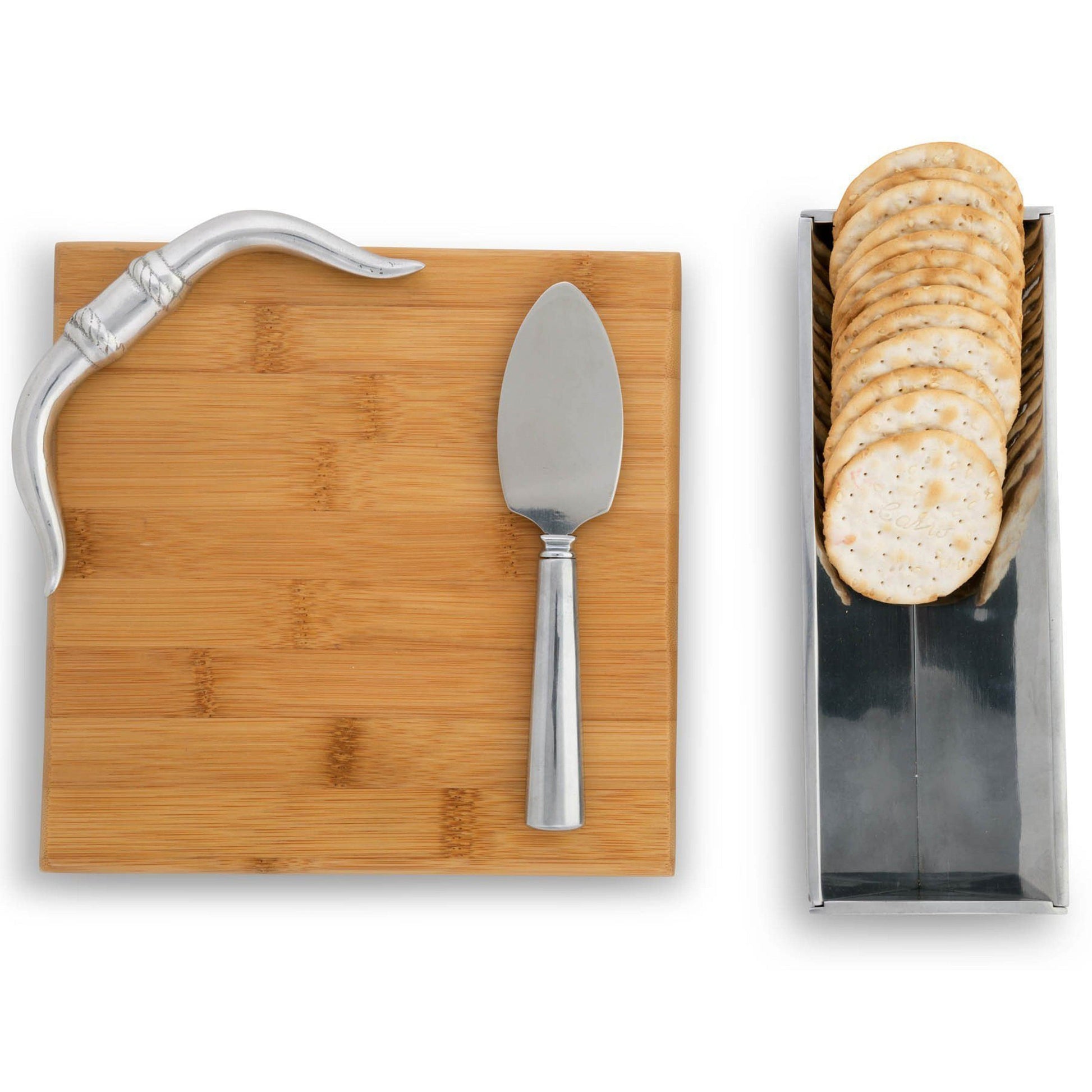 Bamboo cutting board with knife, cheese spreader, and a container of crackers on a white background