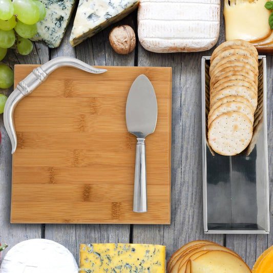 Wooden cutting board with a knife, surrounded by cheeses, grapes, and crackers on a wooden surface.